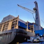 A cargo ship docked in with a crane preparing to remove containers