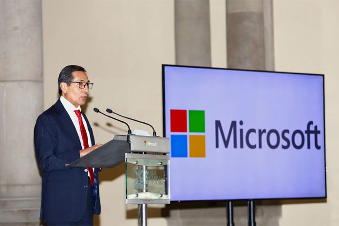 Mexico Finance Minister Rogelio Ramirez de la O standing at a podium beside a large monitor that bears the name and logo of Microsoft