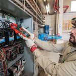 A Mexican electrician holding a digital monitor in front of a geothermal system